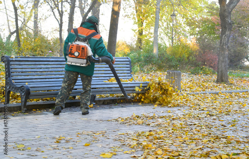 Cleaning up a city square from fallen autumn leaves with backpack leaf blower. photo