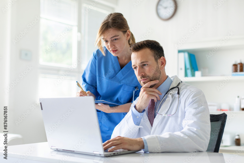 Focused doctor and assistant looking at laptop screen, discussing patient's diagnosis, working together in clinic office Focused doctor and assistant looking at laptop screen, discussing patient's diagnosis, working together in clinic office