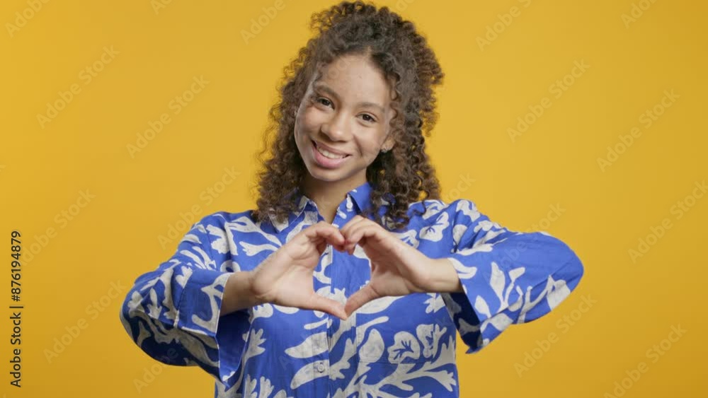 Teenager zoomer girl showing sign of shape heart. Positive lady on yellow. Love.