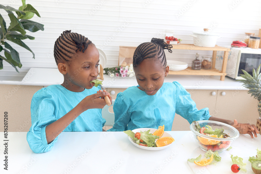 Twin sister kid girl with curly hair braid African eating fresh vegetables and fruits after washing and cleaning in glass bowl for making salad. Cute children preparing salad healthy food at kitchen. Twin sister kid girl with curly hair braid African eating fresh vegetables and fruits after washing and cleaning in glass bowl for making salad. Cute children preparing salad healthy food at kitchen.