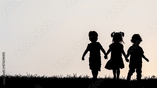 Silhouette of three children holding hands, walking on grass against sunset, symbolizing friendship and innocence. © Sorat