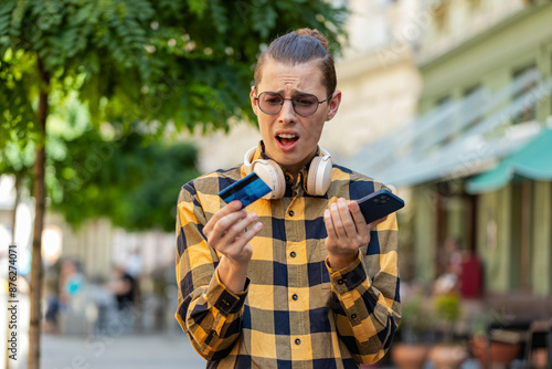 Shocked Caucasian man trying to pay online shopping with smartphone blocked credit card. Annoyed young tourist guy on street buying bank refuse problem unsuccessful payment lack of money balance.