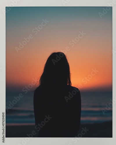 A silhouette of a woman standing on the beach at sunset, gazing at the colorful horizon over the ocean.