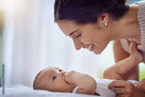 Happy mother, playing and care with baby on bed for love, motherhood or bonding at home. Mom with smile for little todder, newborn or infant in bedroom for family time, holiday or weekend at house photo