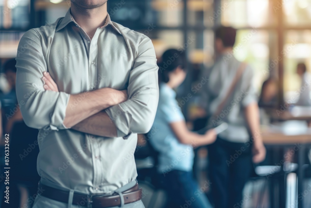 A man in a light shirt stands confidently with his arms crossed in a busy office environment A man in a light shirt stands confidently with his arms crossed in a busy office environment