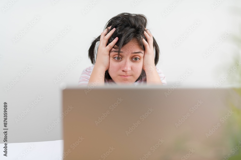 Young student frustrated in front of the computer with hand on head and a white wall background Young student frustrated in front of the computer with hand on head and a white wall background