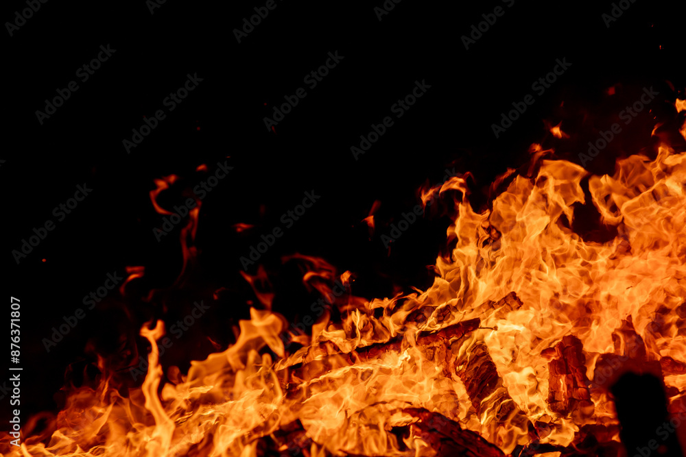 Obraz premium A dramatic image of a fierce fire burning intensely against the dark night sky. The bright orange and yellow flames highlight the raw energy and destructive power of the blaze. Copy space available.