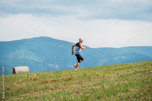 man runs uphill on grassy hill with scenic mountains in background embodying spirit of trail running and ultramarathon training. Landscape create inspiring and dynamic scene depicting extreme sports photo