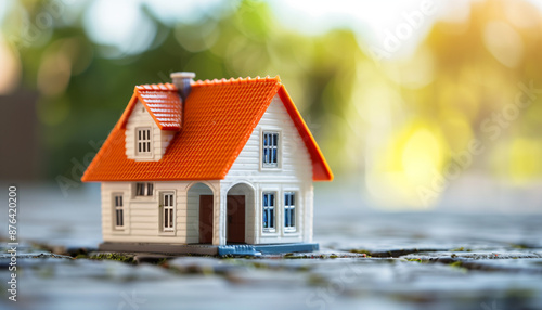 Small model house with a red roof set on a cobblestone path with blurred greenery in the background.