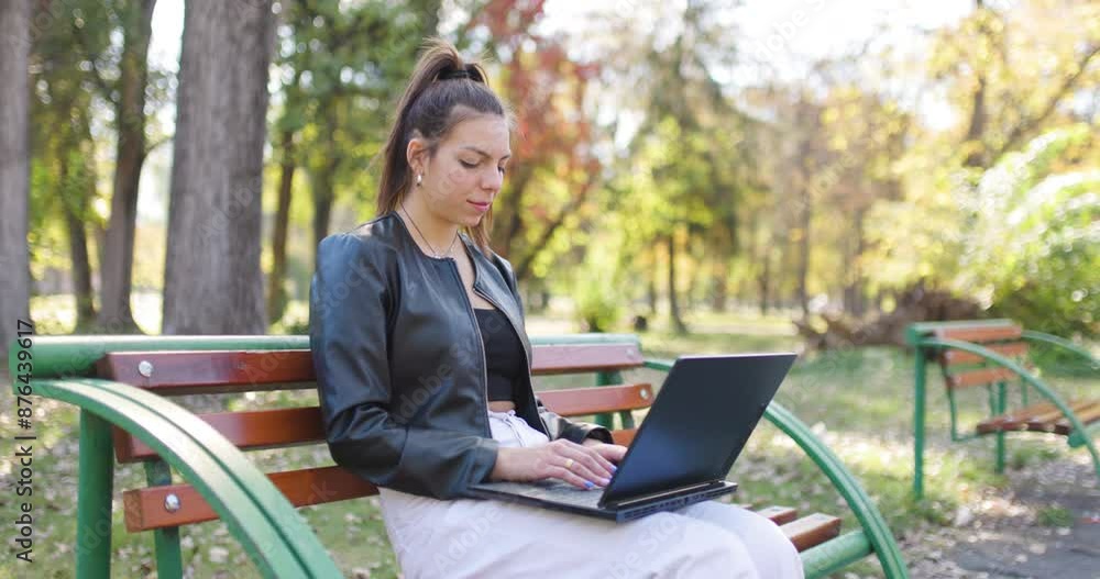 Portait of a fashionable young lady working on a laptop. Beautiful girl sitting on a bench in the park. Portait of a fashionable young lady working on a laptop. Beautiful girl sitting on a bench in the park.