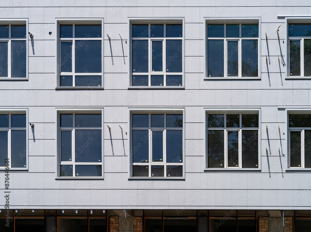 Several windows on the wall of a building with a white facade. .New windows have been installed in a house under construction with a light, ventilated facade. Front view, close-up. Several windows on the wall of a building with a white facade. .New windows have been installed in a house under construction with a light, ventilated facade. Front view, close-up.