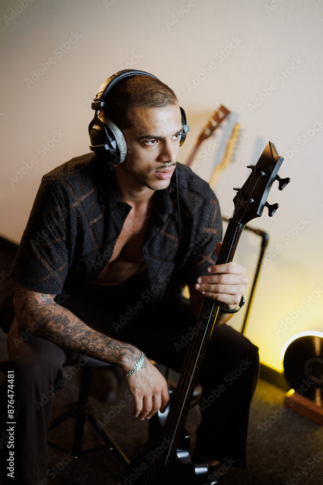 Obraz premium Portrait of stylish guitarist in headphones holding bass guitar in music studio