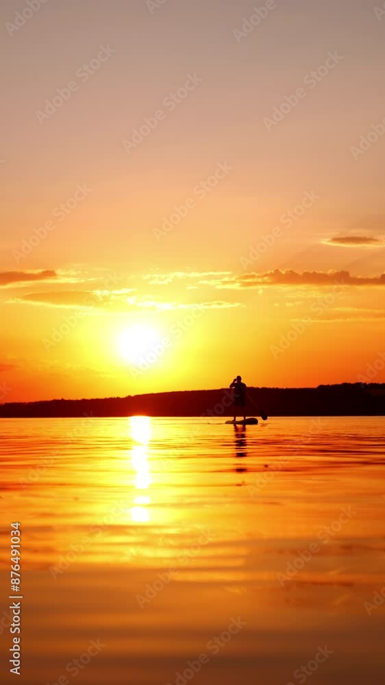 Bright orange sun reflects in the river at sunset. Lonely man oars standing on the sup board approaching camera. Low angle view. Vertical video. Bright orange sun reflects in the river at sunset. Lonely man oars standing on the sup board approaching camera. Low angle view. Vertical video.
