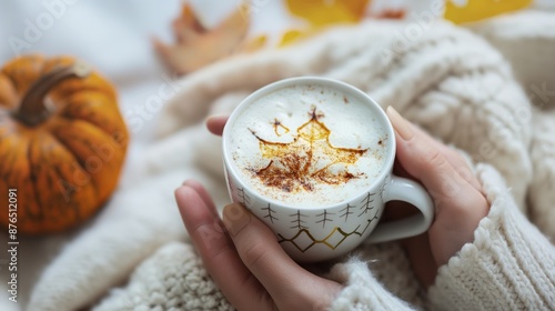 Autumn themed still life with a cozy cup of coffee featuring a foam maple leaf design, a pumpkin, and colorful fall leaves on a white background. photo