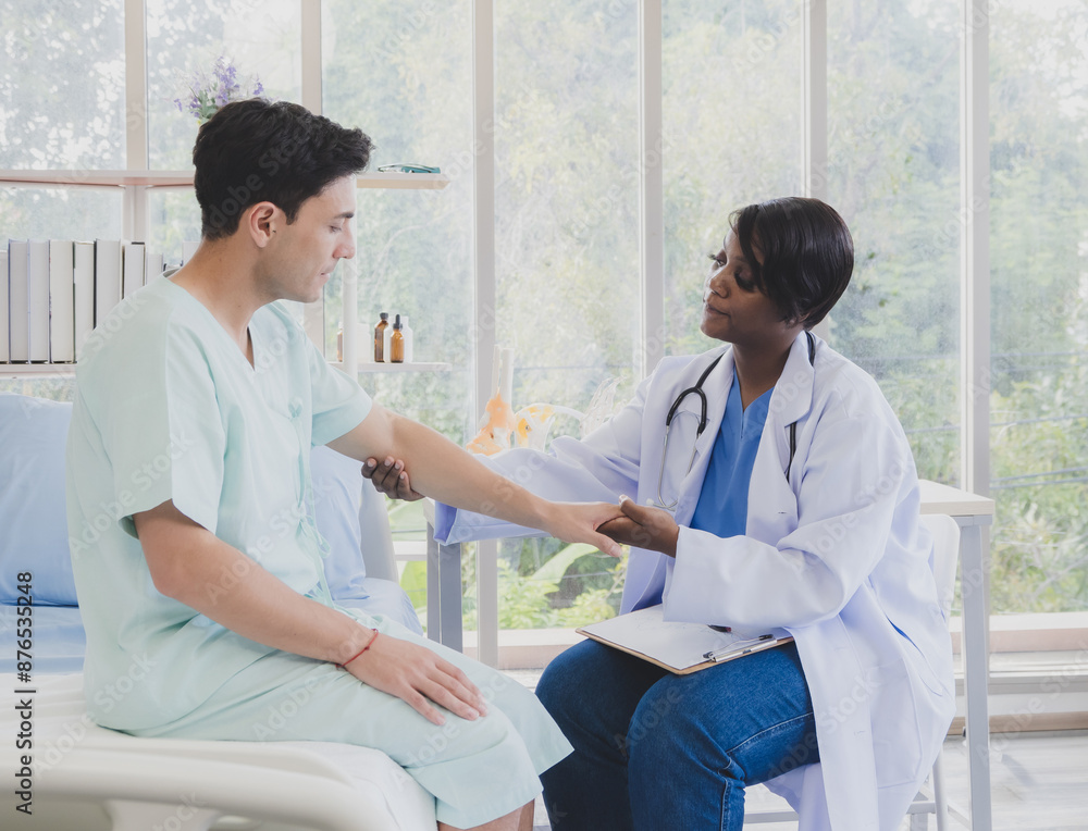 Patient caucasian man with woman nurse carer physical therapist black people two person sitting talk helping support give advice and holding hand arm inside clinic hospital indoor room service. Patient caucasian man with woman nurse carer physical therapist black people two person sitting talk helping support give advice and holding hand arm inside clinic hospital indoor room service.