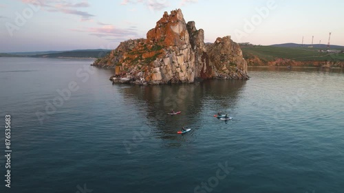 Shamanka Rock, Lake Baikal on a summer evening. Tourists on Sap boards swim in the bay photo