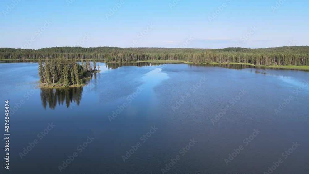 A drone aerial view moving forward over a dark blue colored northern lake under a blue sky. The shore and a small island are covered in a dense forest of spruce and pine trees.
A drone aerial view moving forward over a dark blue colored northern lake under a blue sky. The shore and a small island are covered in a dense forest of spruce and pine trees.