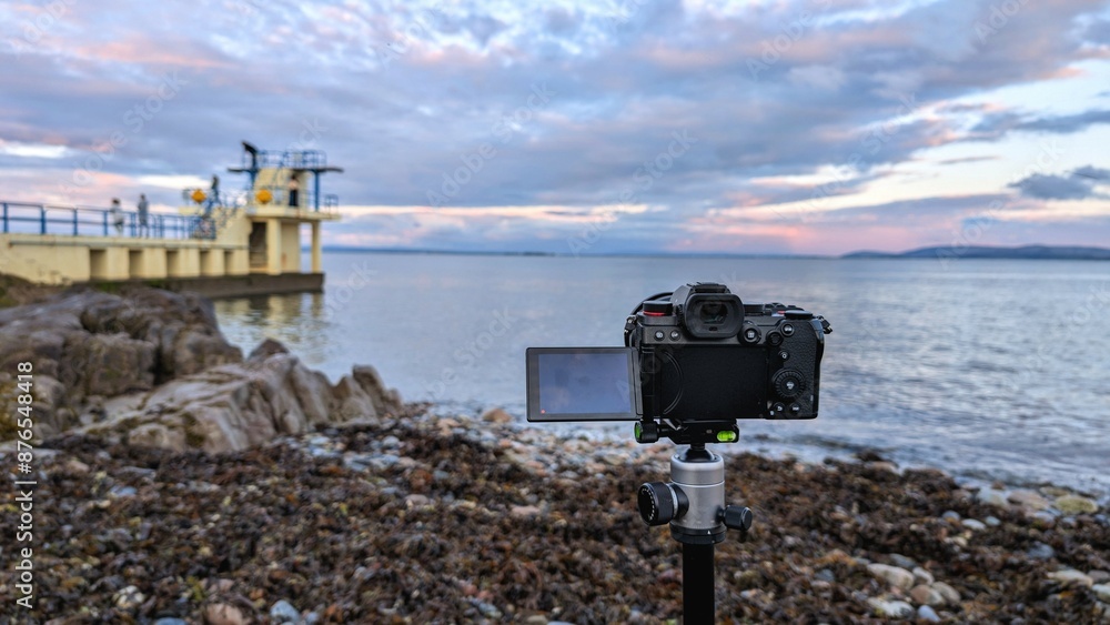 Closeup of modern mirrorless dslr camera recording beautiful scene of Blackrock, Salthill at sunset at Galway, ireland, technology concept background