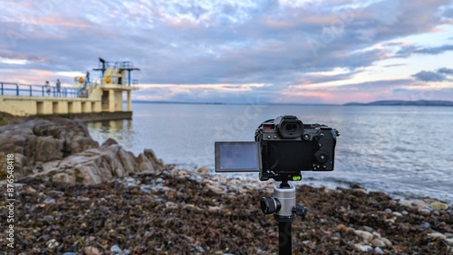 Obraz na płótnie Closeup of modern mirrorless dslr camera recording beautiful scene of Blackrock, Salthill at sunset at Galway, ireland, technology concept background
w salonie