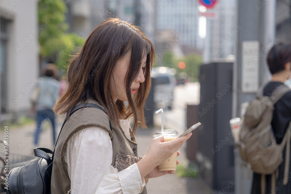 In early summer, a young Chinese exchange student in her twenties, walking around the city near Hamamatsucho, Minato, Tokyo, holding an iced café au lait in a plastic cup in one hand. In early summer, a young Chinese exchange student in her twenties, walking around the city near Hamamatsucho, Minato, Tokyo, holding an iced café au lait in a plastic cup in one hand.