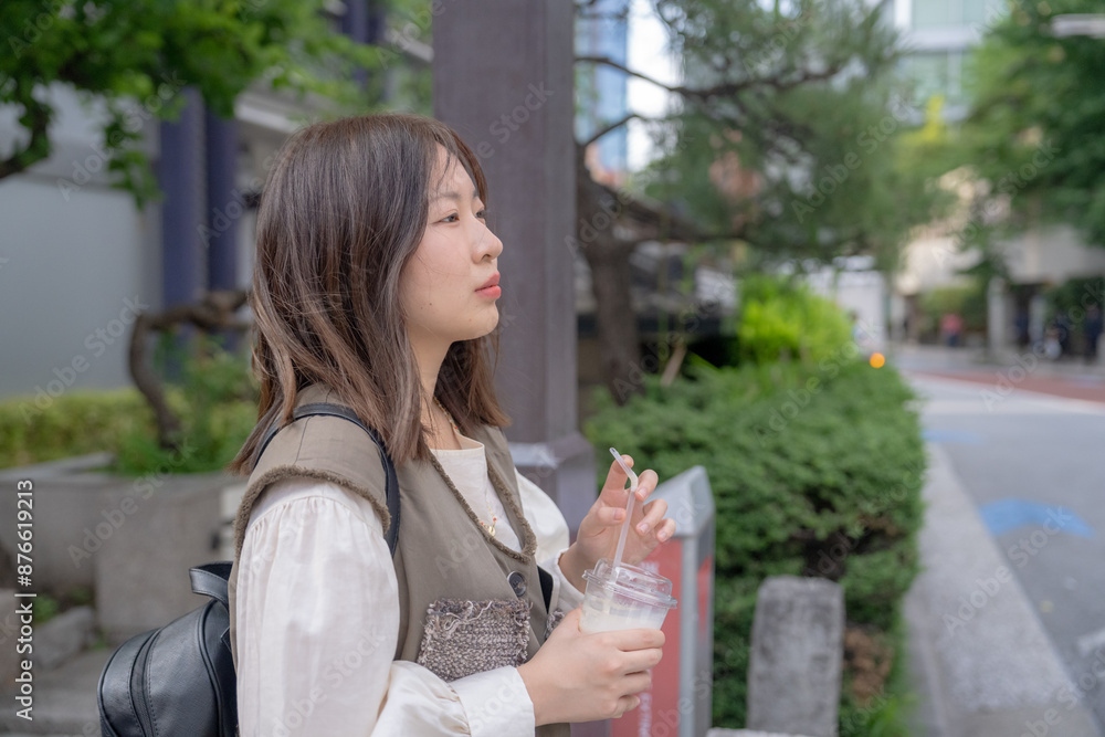 In early summer, a young Chinese exchange student in her twenties, walking around the city near Hamamatsucho, Minato, Tokyo, holding an iced café au lait in a plastic cup in one hand. In early summer, a young Chinese exchange student in her twenties, walking around the city near Hamamatsucho, Minato, Tokyo, holding an iced café au lait in a plastic cup in one hand.