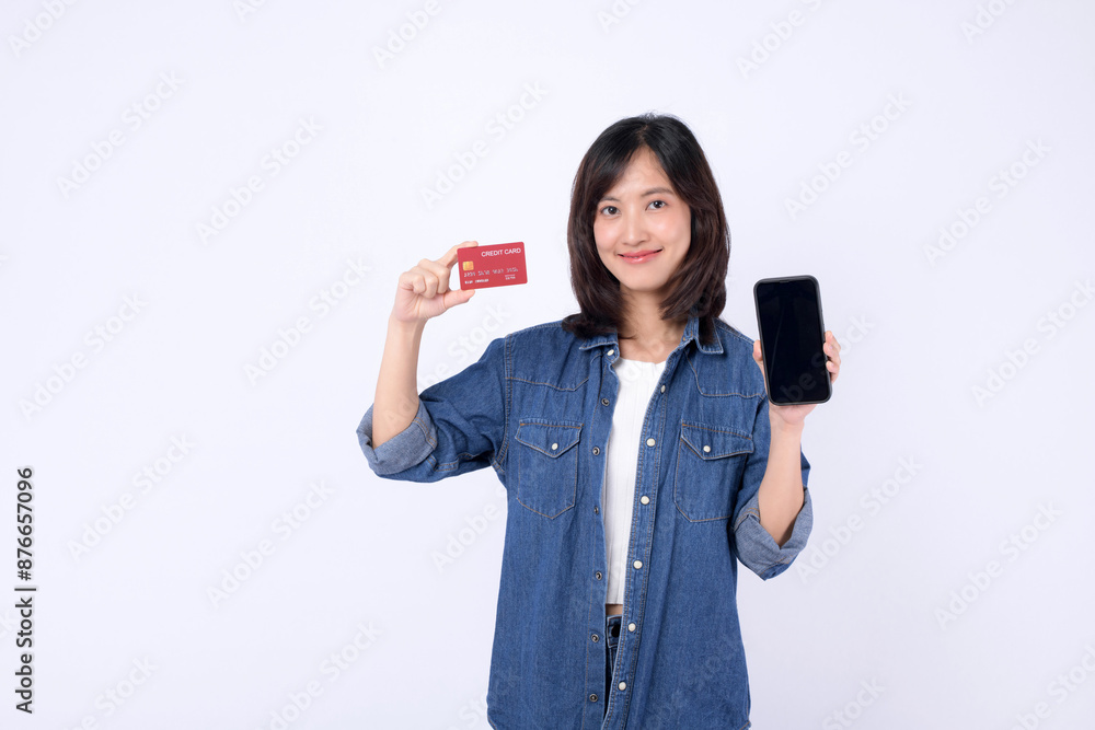 An Asian woman wearing denim jean is holding credit card and a mobile phone against a white background, shopping online concept. An Asian woman wearing denim jean is holding credit card and a mobile phone against a white background, shopping online concept.