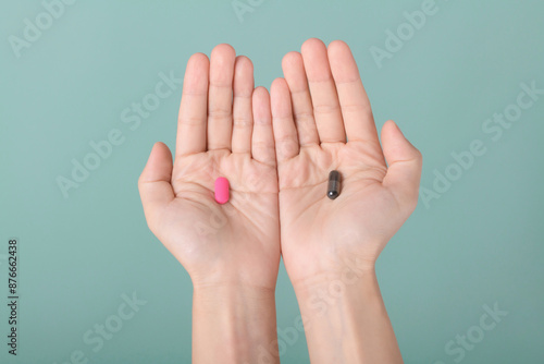 Female hands hold and offer two choice medicine pills capsule for chosen. Black and pink candy or meds compare to choose from. Concept decision making or indecisiveness.