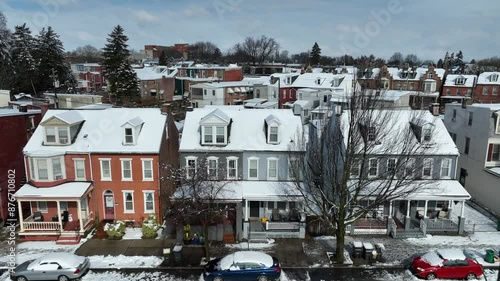 Aerial approaching shot of snowy row of houses and car on street. American neighborhood with snow-covered roofs on sunny day. photo