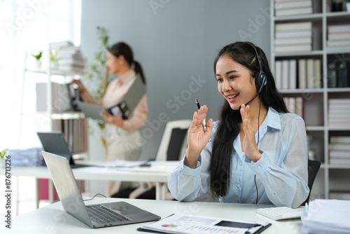 Asian businesswoman employee or executive using laptop computer and wearing headset video call explaining online meeting or online training. Document work in the office.