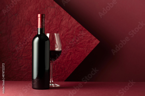 Bottle and glass of red wine on a red background.