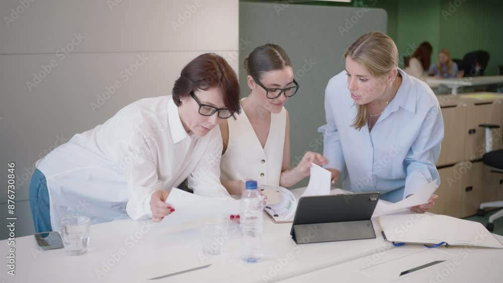 Three professionals are collaborating in a meeting, discussing documents and using a tablet in a modern office. They aim to enhance efficiency through teamwork and innovative ideas Three professionals are collaborating in a meeting, discussing documents and using a tablet in a modern office. They aim to enhance efficiency through teamwork and innovative ideas