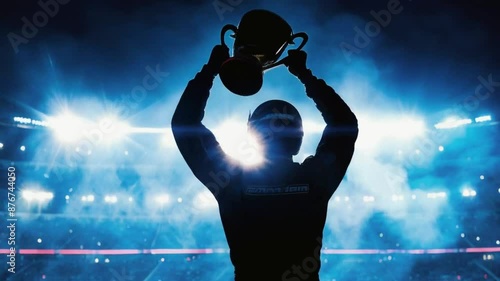 Silhouette of a race car driver celebrating the win in a race against bright stadium lights, raising a trophy over his head