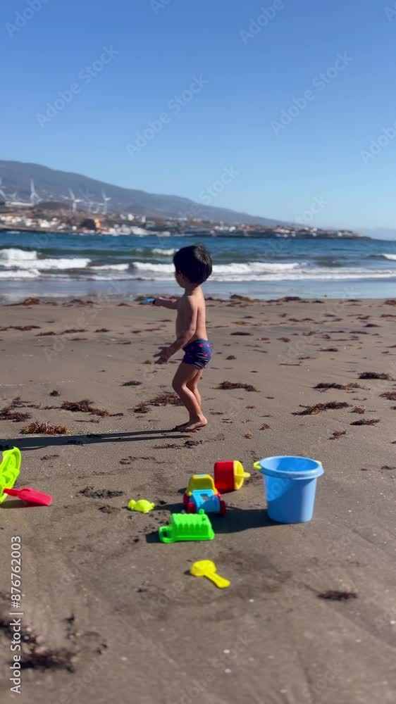 Boy alone playing with shovel pouring sand into bucket on beach on summer vacation Boy alone playing with shovel pouring sand into bucket on beach on summer vacation