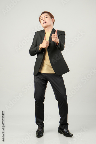 full length shoot of cheerful happy asian business man wearing suit with pointing finger hand gesture on isolated background