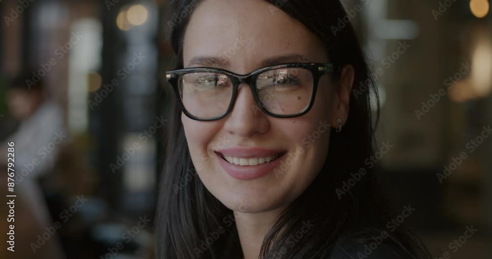 Close-up slow motion portrait of cheerful young businesswoman turning to camera and smiling indoors in cafe. Ambitious person and positive emotion concept. Close-up slow motion portrait of cheerful young businesswoman turning to camera and smiling indoors in cafe. Ambitious person and positive emotion concept.