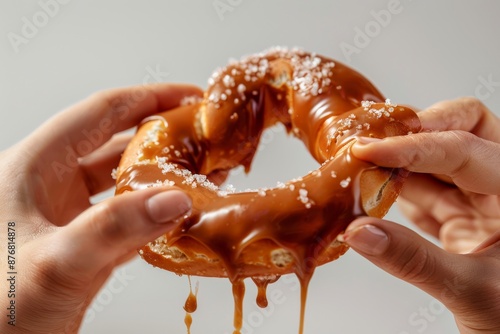 Hands pulling apart a freshly baked pretzel covered in rich, melted caramel, revealing the soft, doughy texture underneath
