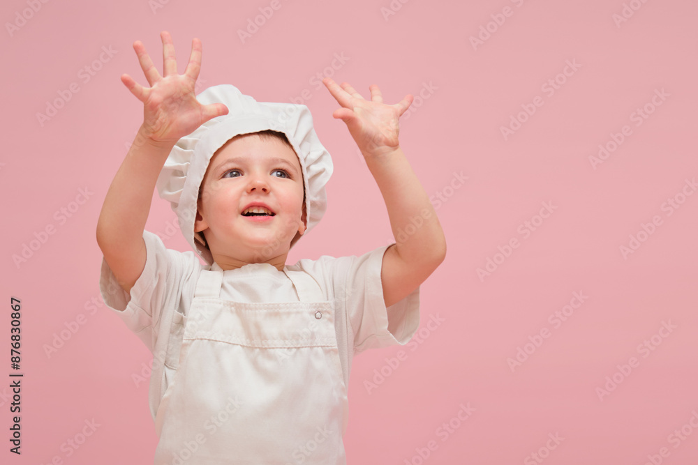 Happy child shows the number 10, dressed as a chef in a white uniform, looks adorable in a childhood portrait with a pink background. Kid aged 3 years (three year old boy)
