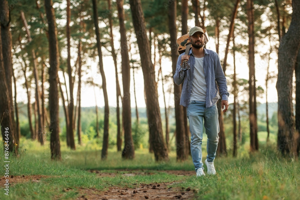 Walking forward. Handsome man is in the forest with acoustic guitar Walking forward. Handsome man is in the forest with acoustic guitar