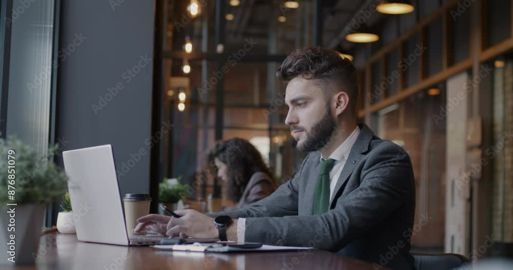 Side view of young businessperson working with computer typing browsing sitting in cafe with group of people. Businessman and modern lifestyle concept. Side view of young businessperson working with computer typing browsing sitting in cafe with group of people. Businessman and modern lifestyle concept.