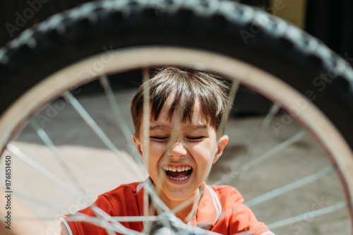 Cheerful boy with eyes closed behind bicycle wheel photo