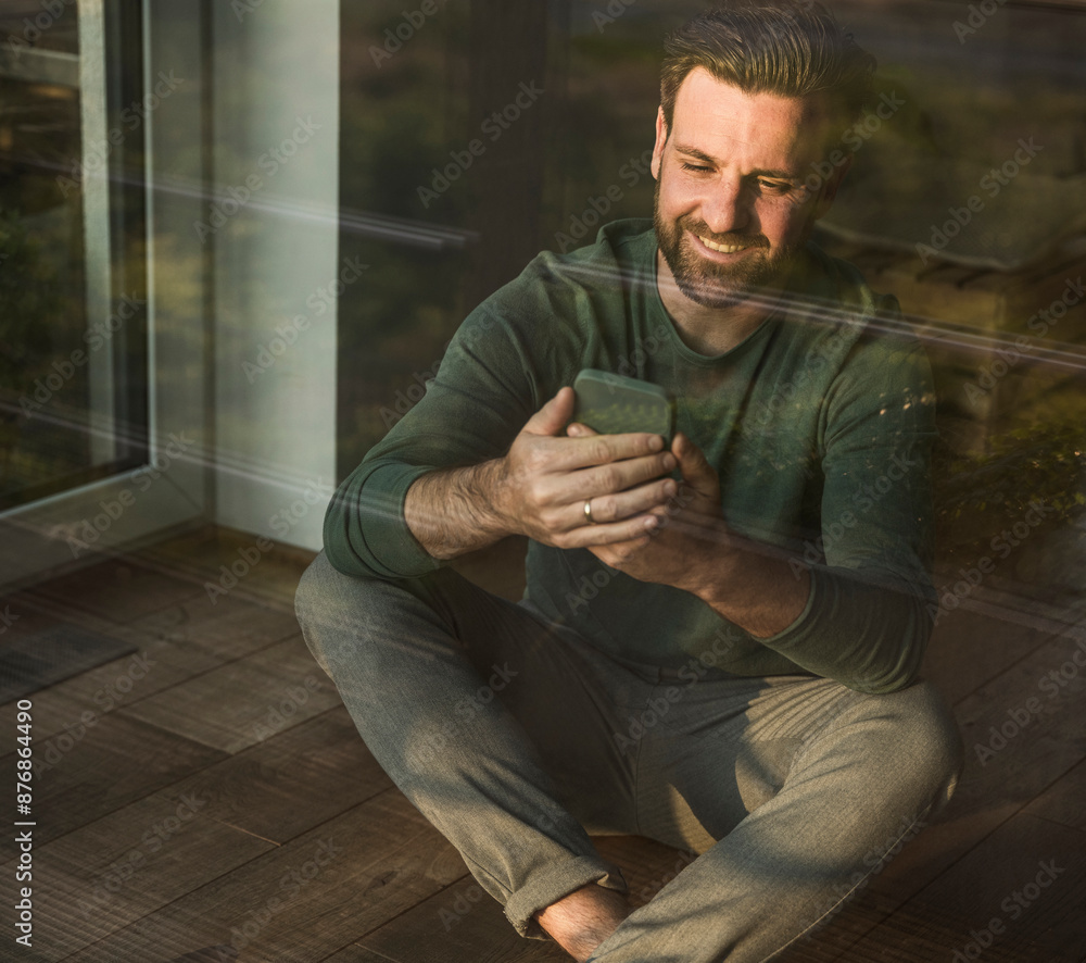 Smiling man using smart phone sitting at home Smiling man using smart phone sitting at home