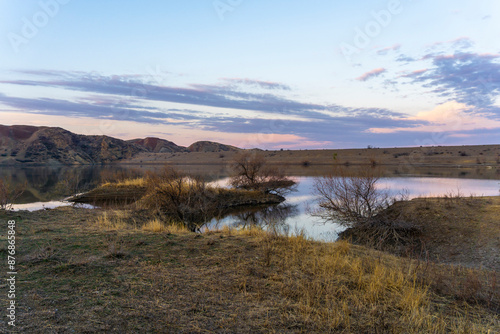 Before sunrise at the reservoir. Blue sky and mountains reflected in the water. Islands grass and bushes