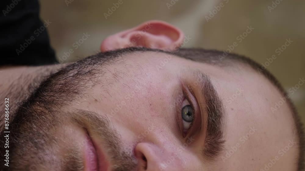 A vertical close-up of a young man with light beard stubble, showing only half of his serious face. His intense gaze and focused expression dominate the frame A vertical close-up of a young man with light beard stubble, showing only half of his serious face. His intense gaze and focused expression dominate the frame