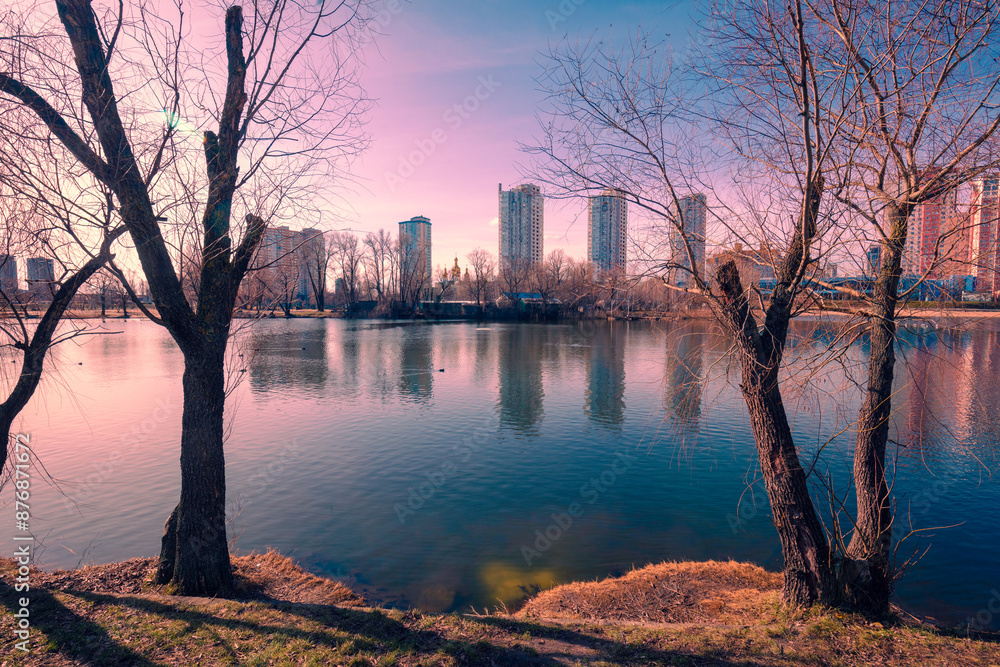 Kyiv in the morning. Left bank of the Dnieper River. Lakeshore with trees in the evening. Beautiful reflection of buildings in the lake