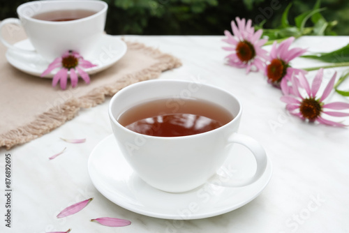 Cups of healthy echinacea tea, coneflower herbs and on a light table. Side view.