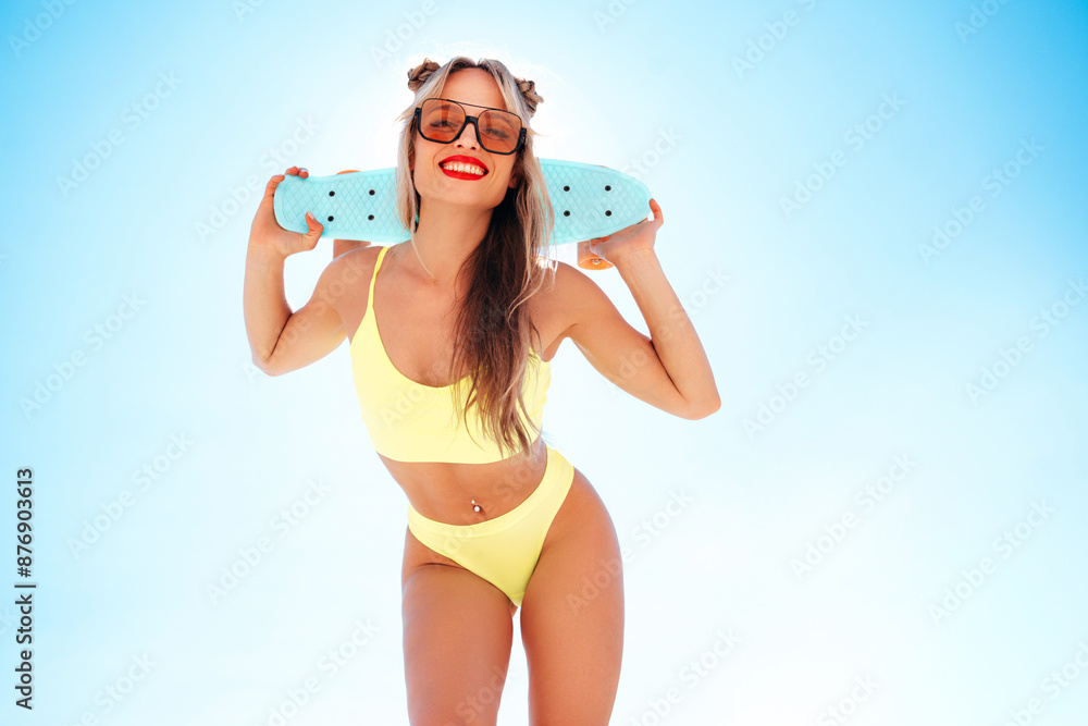 Young beautiful smiling blond woman posing in the street in sunny day. Sexy model in swimwear bathing suit. Positive female with red lips. Holding penny skateboard. Happy and cheerful, blue sky behind Young beautiful smiling blond woman posing in the street in sunny day. Sexy model in swimwear bathing suit. Positive female with red lips. Holding penny skateboard. Happy and cheerful, blue sky behind