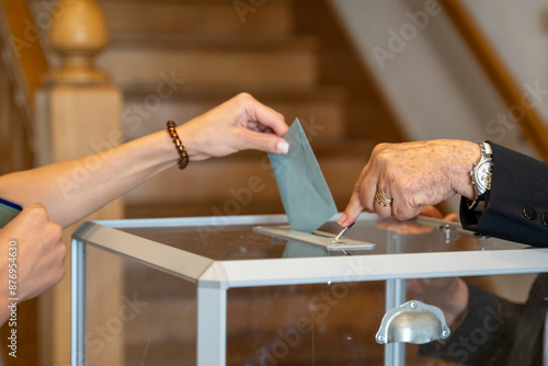 vote en république française, enveloppe glissée dans une urne transparente et ouverte  avec un clapet par un assesseur