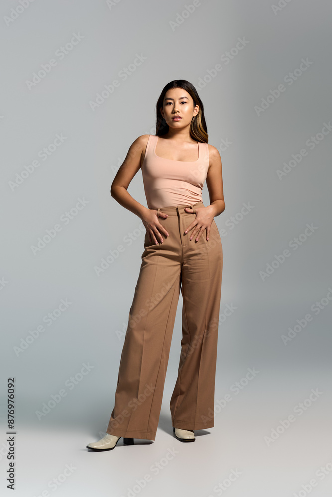 Fototapeta premium A woman in tan trousers and a pink top stands in a studio setting.