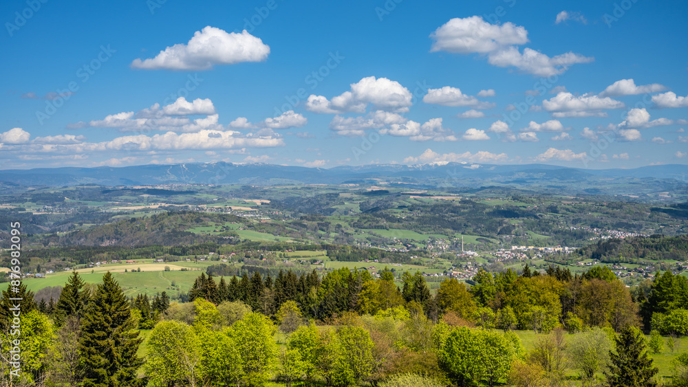Obraz premium A panoramic view of the Krkonose mountains from Kozakov Mountain in the Bohemian Paradise, Czechia. The image captures a sunny day with a clear sky and rolling green hills.