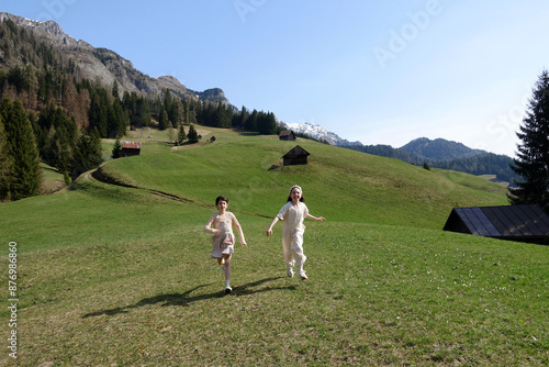 Obraz na plátně Two girls in neutral clothing running down green hills in the dolomites on a sun